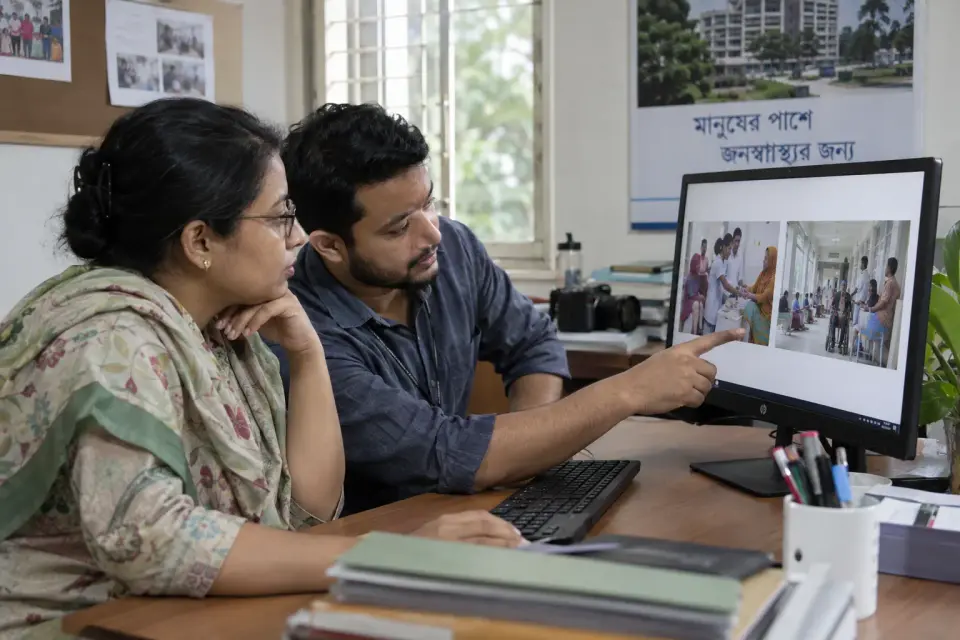 At a agency workstation, a hospital communications manager reviews two neutral campaign-photo mockups with a media specialist.